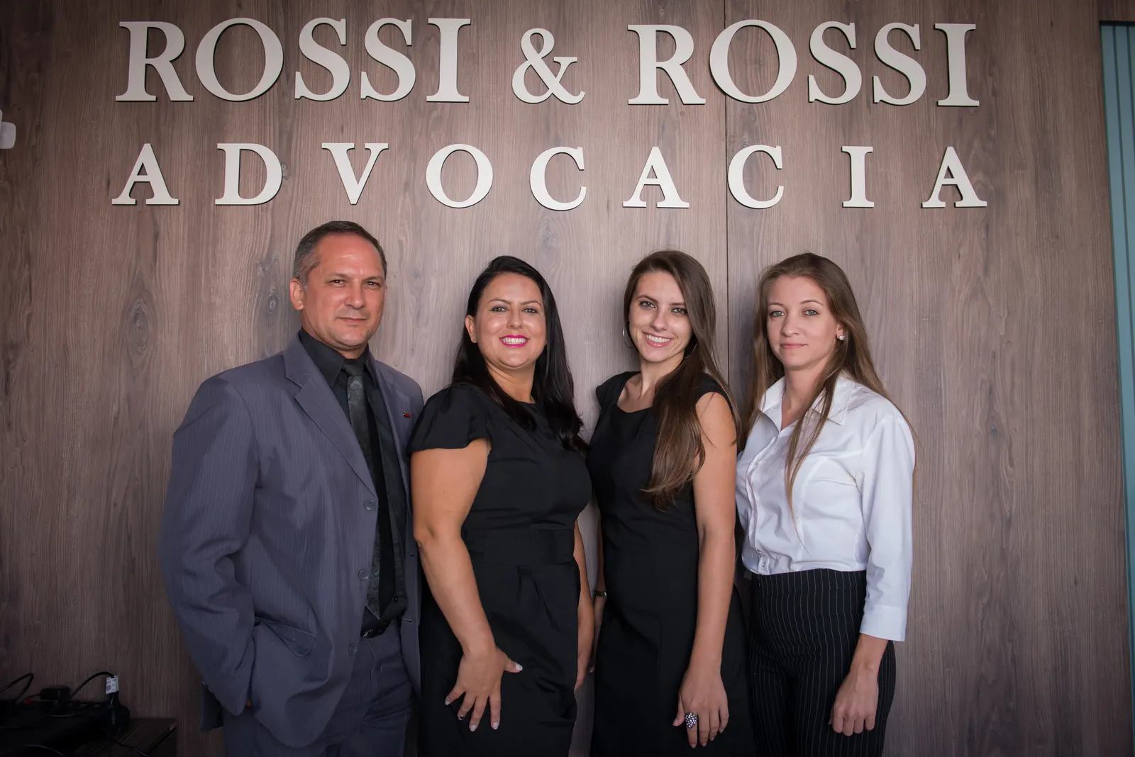 Equipe diante do letreiro Rossi & Rossi Advocacia na parede de madeira